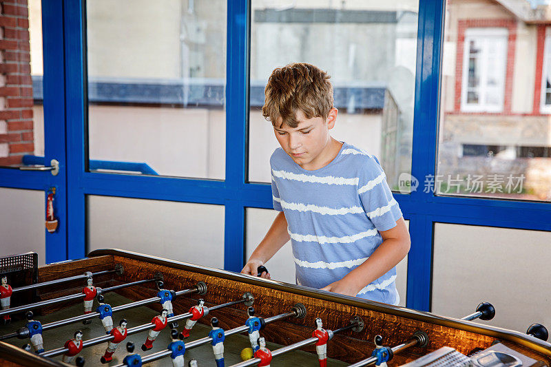 面带微笑的男生踢桌上足球。快乐兴奋的孩子与兄弟姐妹或朋友玩家庭游戏的乐趣。积极的孩子。