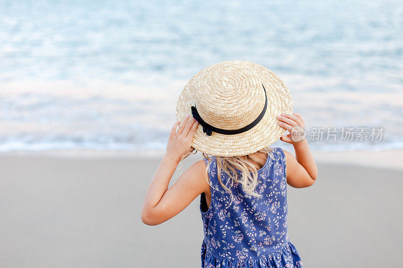 暑假小女孩在海边。戴草帽的可爱小孩是户外度假胜地的游客。儿童假期，旅游，温柔，女性化的概念。孩子在看海景。