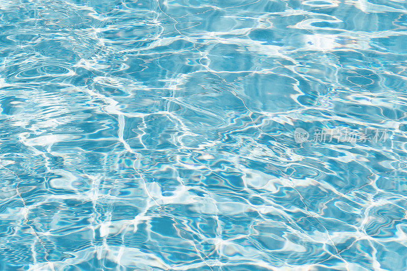清澈的蓝色池水的特写与温柔的涟漪和斑点的阳光。完美的夏季氛围，游泳池广告，或水的背景。