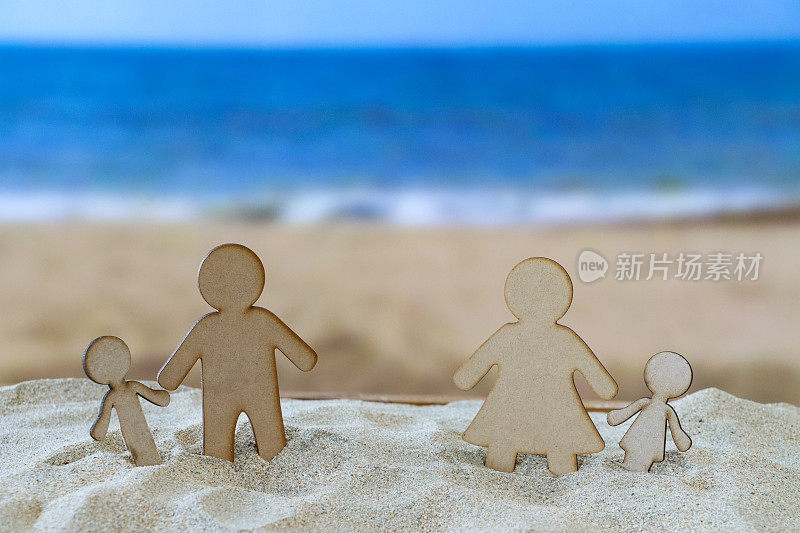 木雕分离家庭在沙堆上的特写形象，父母和孩子，父亲和儿子，母亲和女儿，沙滩背景，海浪在退潮时破碎，大海和海岸线，重点在前景，离婚家庭度假的概念