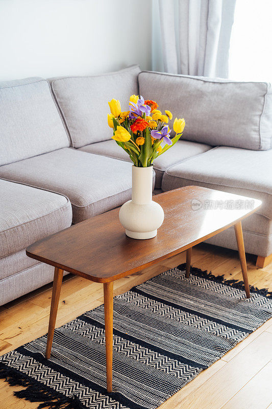 陶瓷花瓶与多色各种花束复古风格的木制咖啡桌与模糊的背景现代舒适的光客厅与灰色沙发沙发。温馨家居室内设计