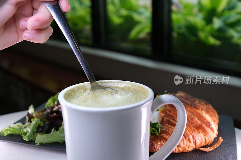 美味的抹茶泡沫用勺子舀起健康的绿茶加牛奶。健康饮食牛角包配奶酪和沙拉，法式早餐，午餐，小吃，晚餐，饮食美味