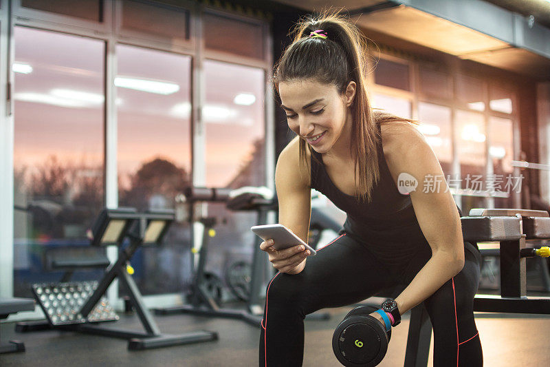 年轻女子在健身房使用手机。