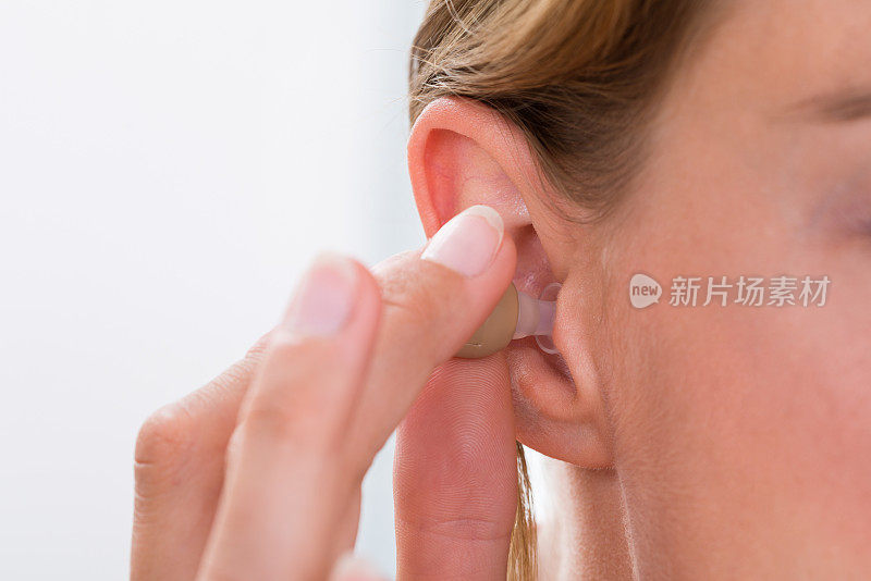 女性的手把助听器放在耳朵里