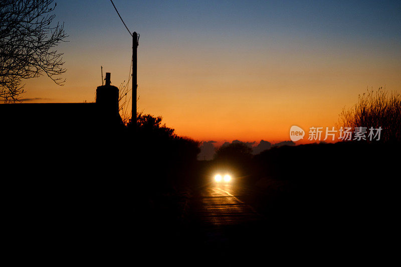 夕阳西下，远处乡间小路上的汽车前灯