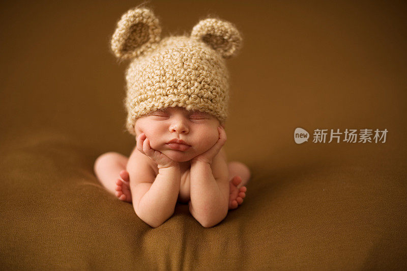 一个新生儿睡在带耳朵的棕色针织帽子里