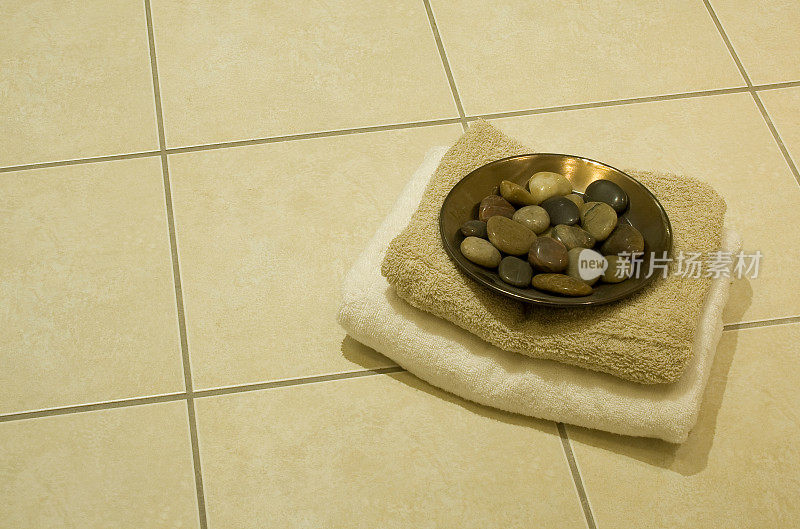 铺着瓷砖的地板上放着毛巾和一盘鹅卵石。
