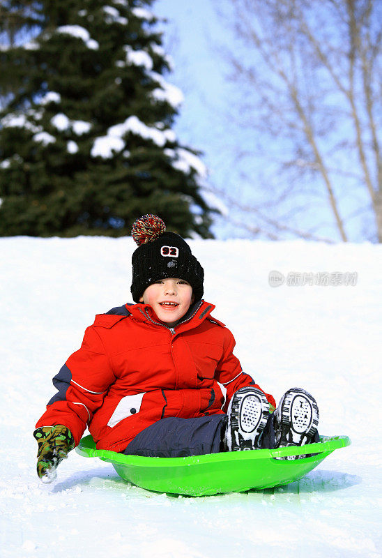 一个快乐的小男孩在雪地里坐雪橇