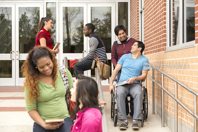 教育:帮助残疾学生下轮椅坡道。大学校园。