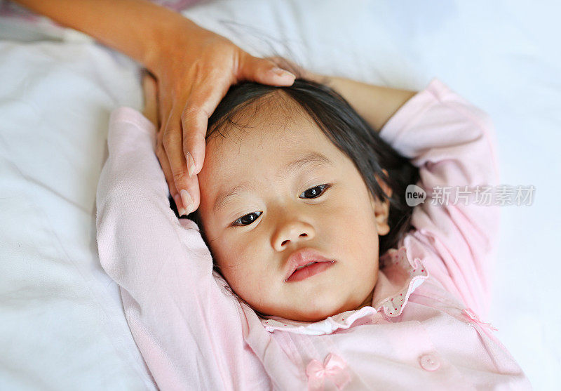 生病的女孩躺在床上用手摸着妈妈的头。
