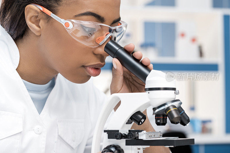 穿着白大褂的非裔美国科学家在化学实验室用显微镜工作