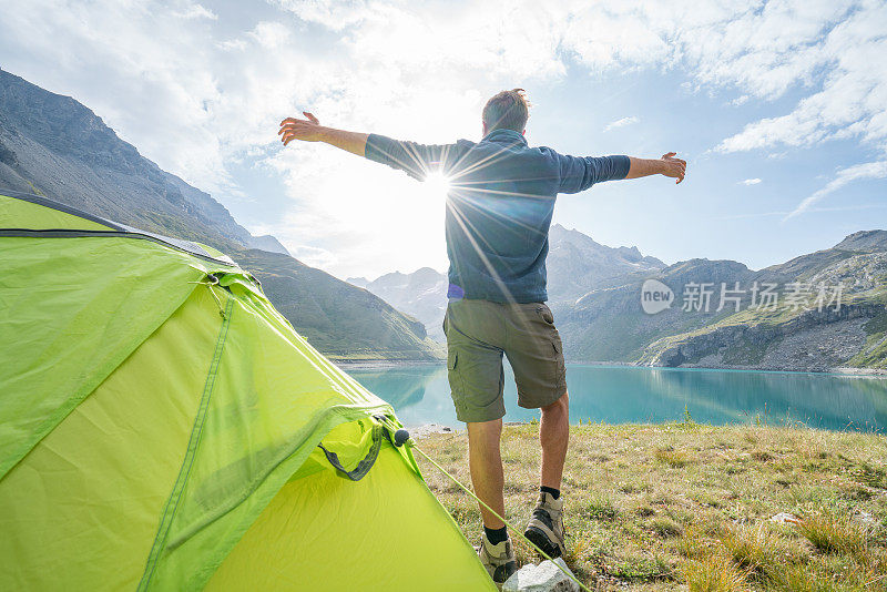 一个年轻人站在帐篷附近，伸开双臂