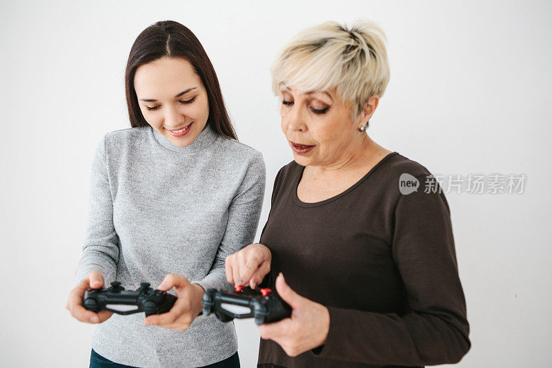 老妇人问小女孩如何使用电子游戏的操纵杆，并在按钮上展示了她的手指。现代技术和人。教老一代使用科技。