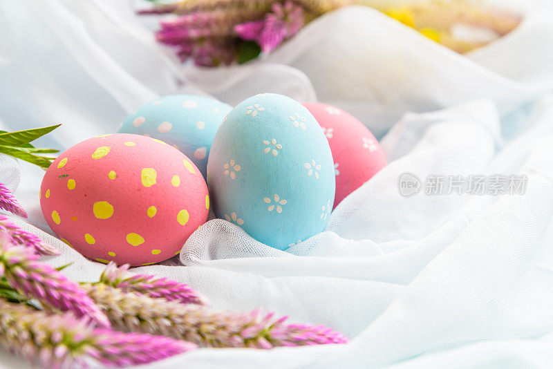 复活节快乐!巢中的复活节彩蛋色彩丰富，以白色的粗棉布为背景，点缀着花朵、纸星星和羽毛。