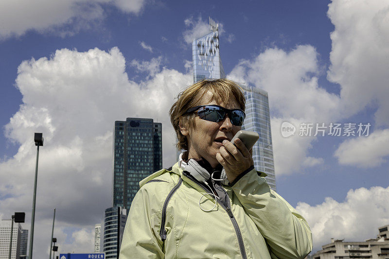 法国巴黎，塞纳河河畔的拉德芳斯，一个成熟的女人在跑步中使用手机