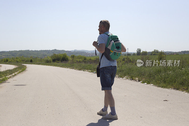 一个成年男子背着背包在镇出口的柏油路上徒步旅行