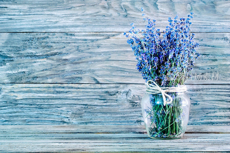 一束薰衣草放在玻璃花瓶里的照片，脖子上缠着粗绳，右边是浅蓝色的木制背景