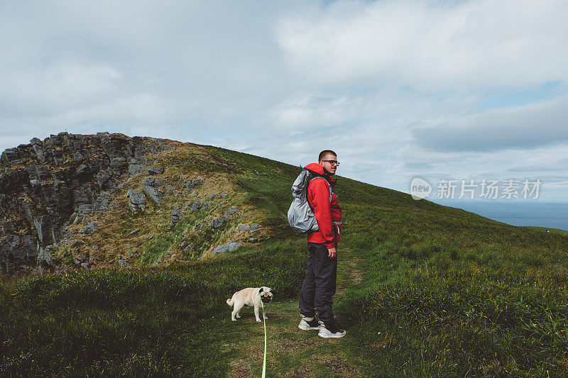 一名男子背着背包和小狗在挪威北部岛屿徒步旅行