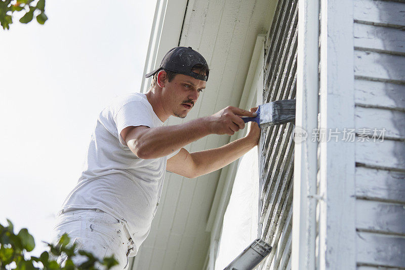 一名男子正在旧房子的外面刷油漆