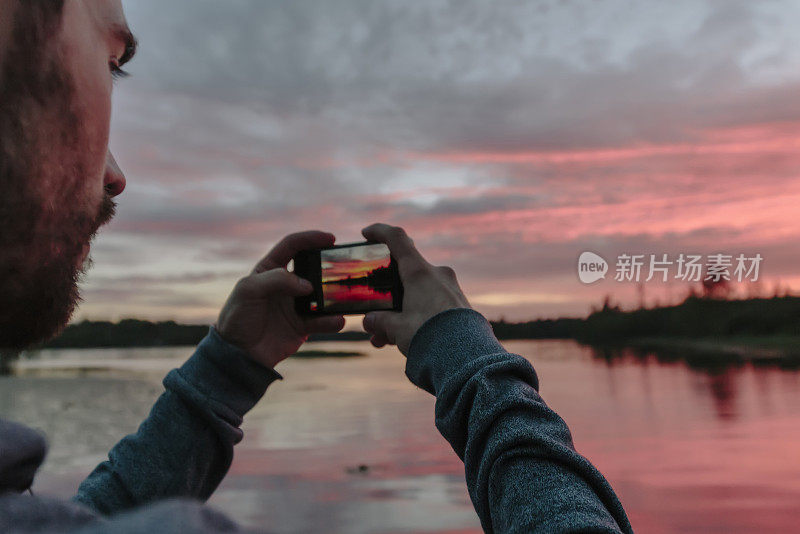 一个男人在湖边拍了一张日落的照片。