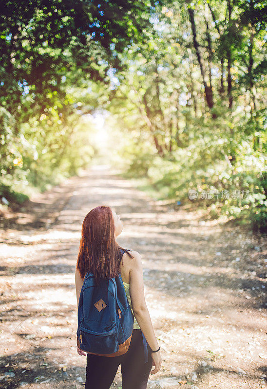 女旅行者背着背包走在森林里的小路上。