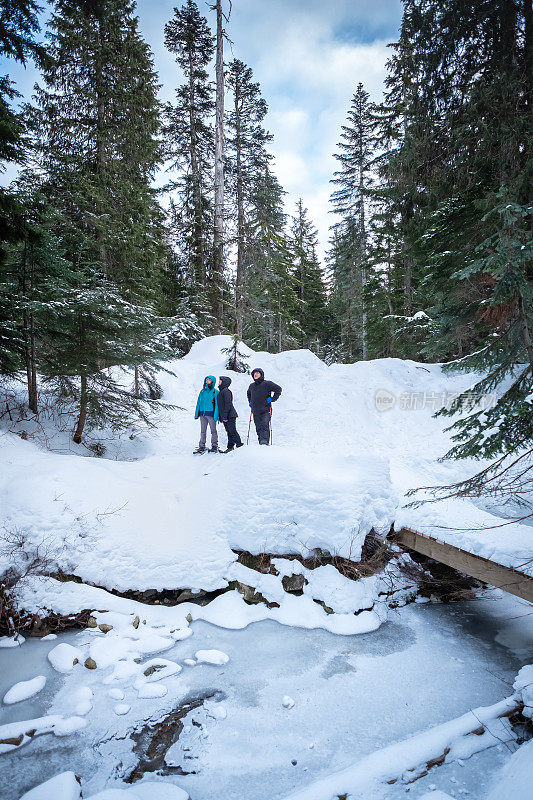 父亲和多民族的女儿在冰冻的小溪边穿雪鞋