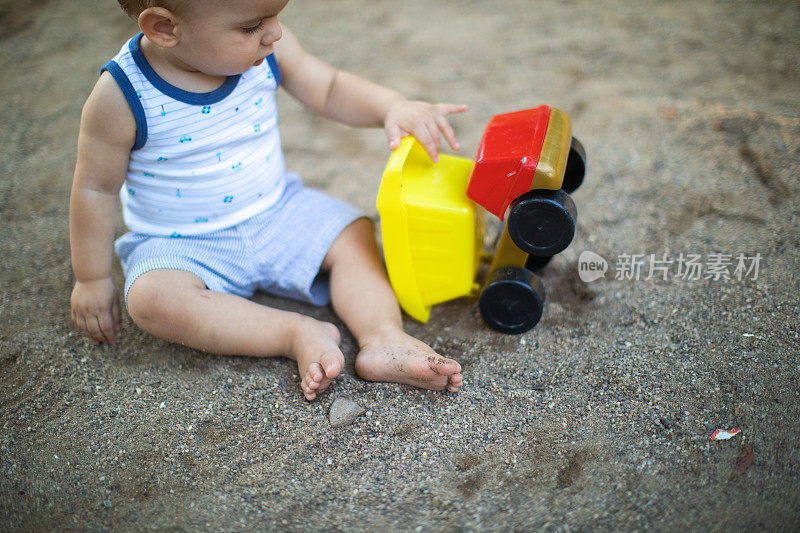 蹒跚学步的小男孩在沙滩上玩玩具卡车