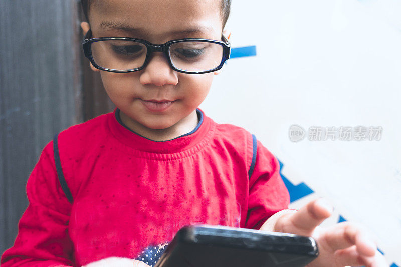可爱的小男孩使用智能手机和戴眼镜