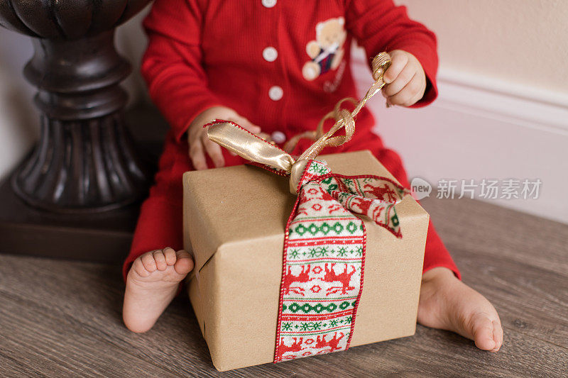 婴儿打开一个圣诞礼物在红色的圣诞睡衣