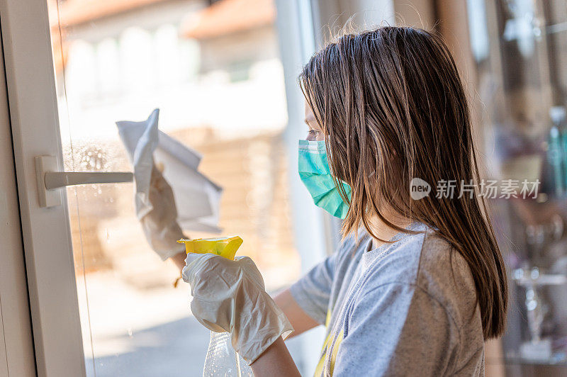 年轻的女孩戴着外科口罩和防护手套在家里擦窗户