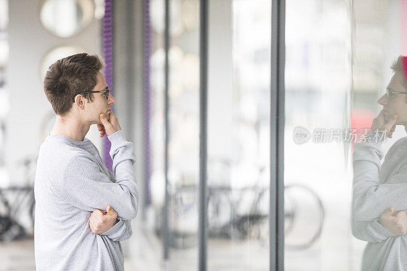 年轻的成年男子看着商店的窗户手在下巴-股票照片