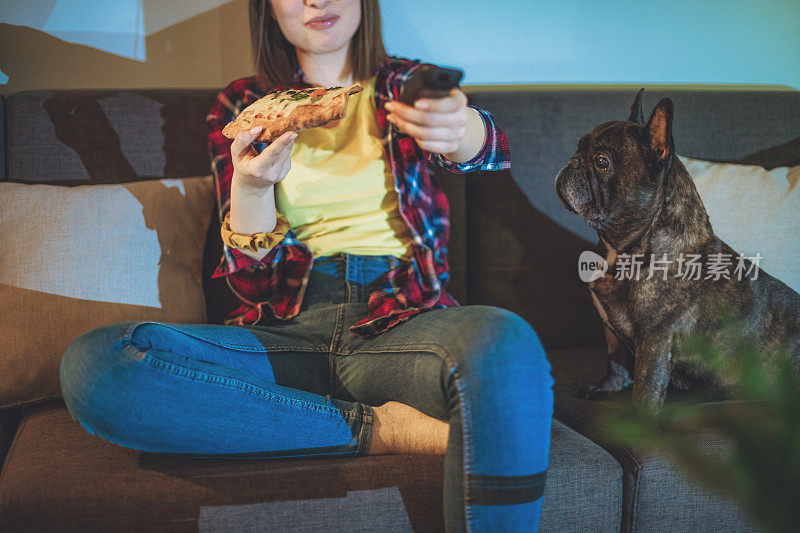 一个女人在沙发上吃披萨，和她的狗一起看电视