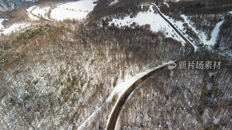 多风的道路在积雪覆盖的森林，从上到下鸟瞰图