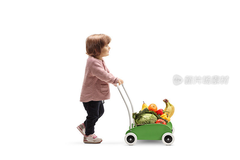 蹒跚学步的小女孩推着一辆装着水果和蔬菜的玩具车