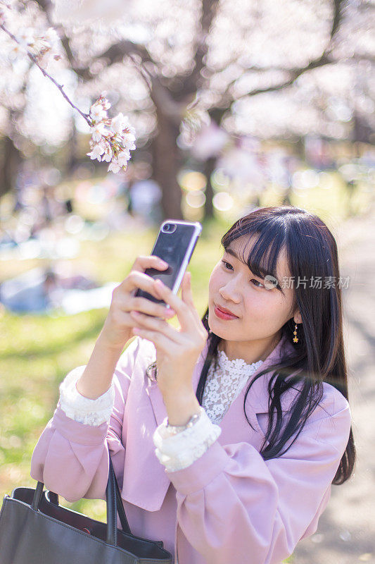 年轻女子在阳光明媚的春天里拍摄樱花的照片