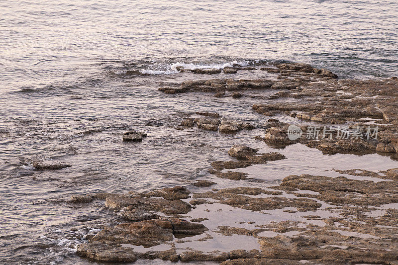 日出时金色阳光下的爱琴海希腊岛的岩石海岸