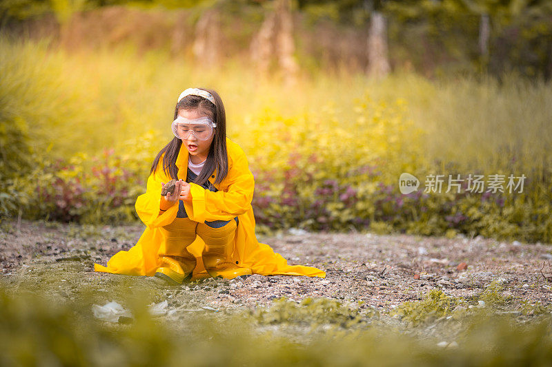 一个亚洲的中国女孩穿着雨衣和农家鞋在农场的草地上玩耍。