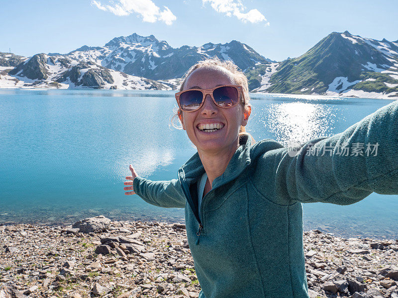 年轻女子在美丽的高山湖周围徒步旅行时自拍