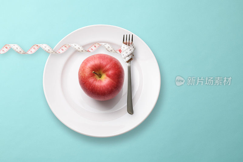 红苹果放在盘子里，用卷尺卷了一把叉子。