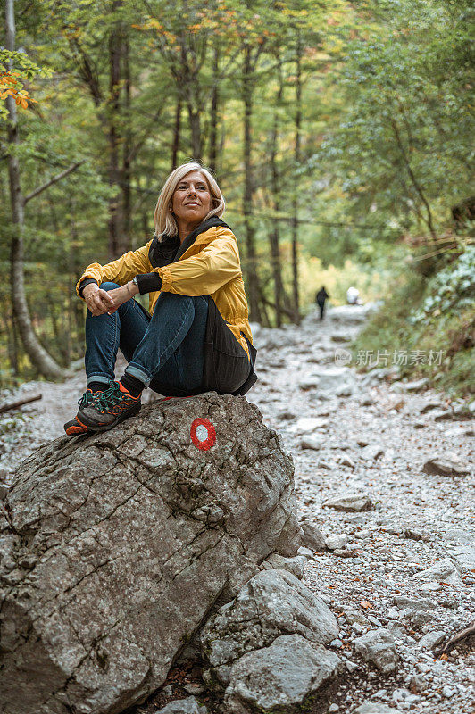 女徒步旅行者坐在树林里的一块大石头上