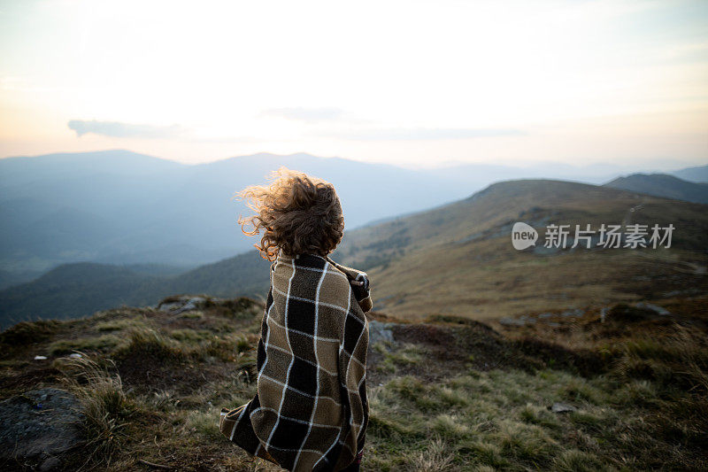 一个美丽的女人的肖像与卷曲的头发被风吹在山日落