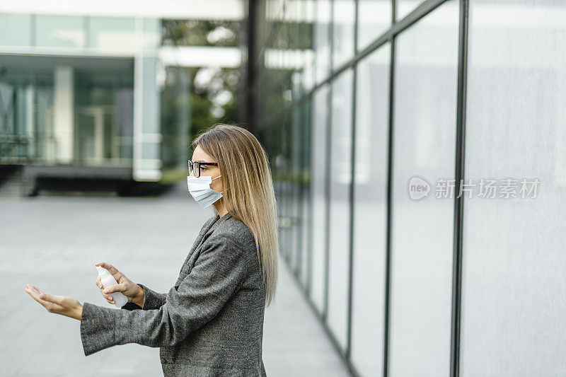 年轻女商人在冠状病毒大流行期间用洗手液洗手并佩戴防护口罩以保护自己