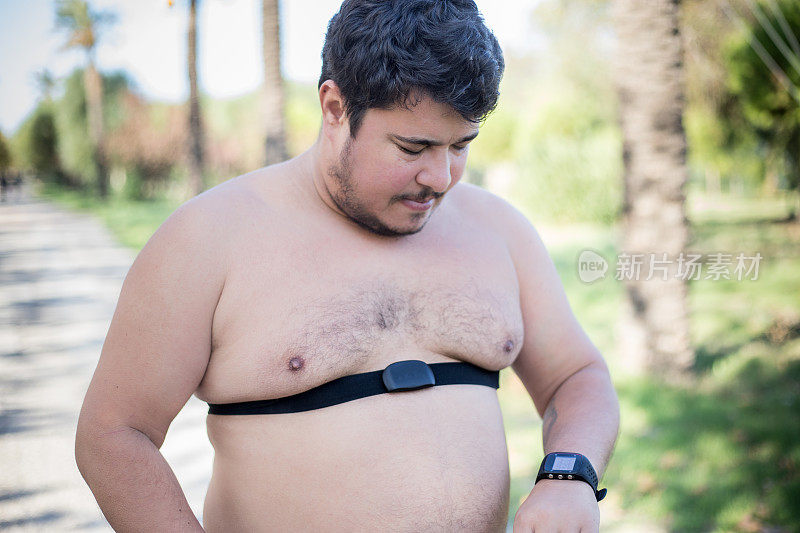 赤裸上身的超重男子戴着胸部心率监测器，准备在公园里锻炼