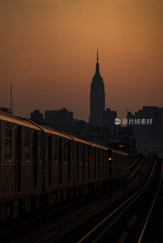 夕阳西下的纽约皇后区地铁列车，以帝国大厦为背景