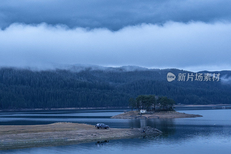 在雾中钓鱼。一辆停在湖岸的秋景车，和一个在水上小岛上移动的家。