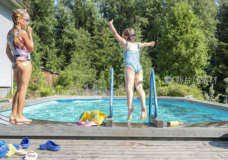 高加索儿童在室外游泳池愉快地游泳。两个女孩，一个6岁，一个8岁，在一个夏日的室外游泳池里游泳。