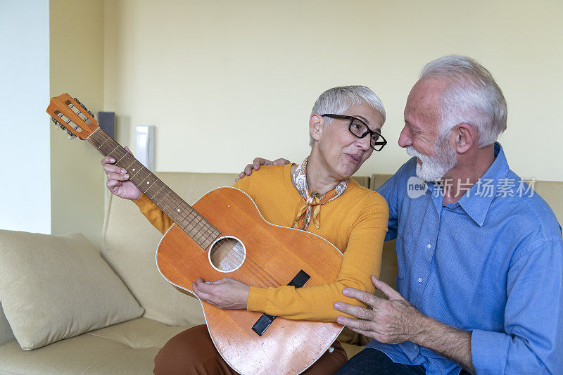 快乐的老女人与吉他是花美好的时间与她的丈夫在客厅舒适的公寓。
