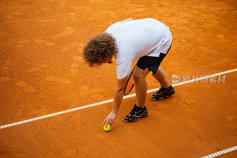在他完成了一次网球练习后，负责任的男网球运动员从球场上捡球
