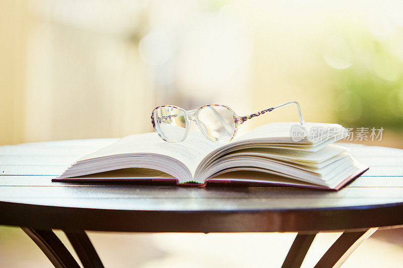在阳光明媚的日子里，带着一副眼镜，在户外的桌子上打开书