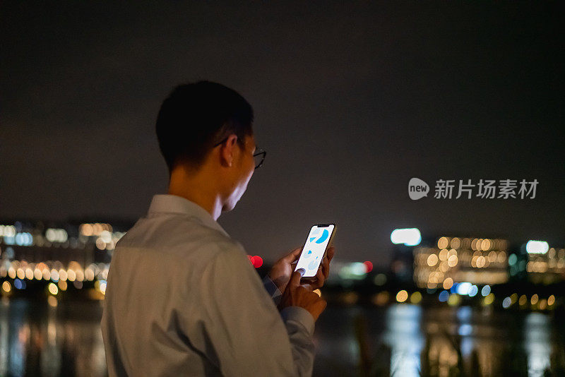 一名亚洲男子晚上在户外使用智能手机